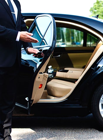 Chauffeur in a suit opening the rear door of a black sedan